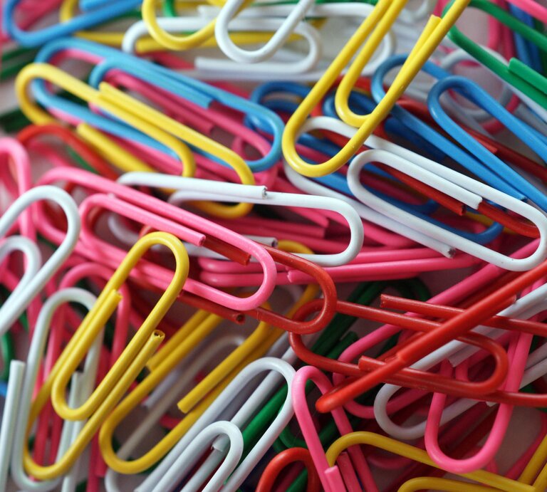 Ein chaotischer Haufen bunter Büroklammern in Gelb, Blau, Rot, Grün, Weiß und Pink, teilweise ineinander verhakt. | © Adobe Stock/cirquedesprit