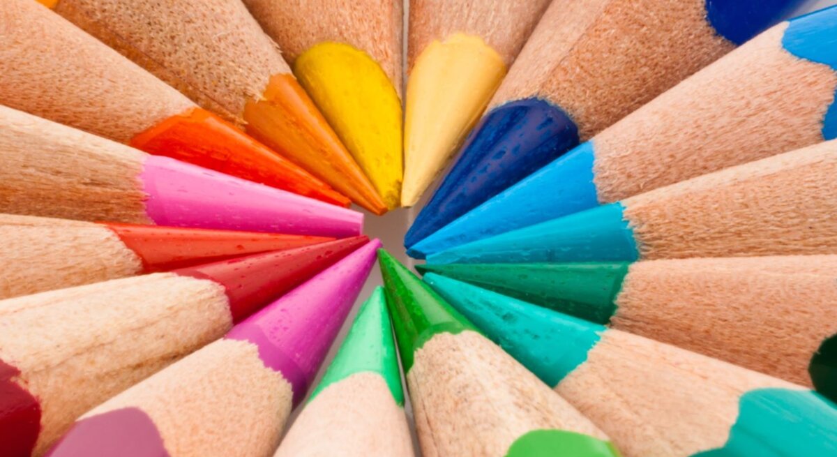 Bunte Buntstifte in kräftigen Farben liegen mit den gespitzten Spitzen fächerförmig auf weißem Hintergrund.