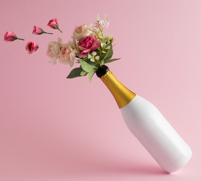Ein kreatives Blumenbouquet mit rosa und cremefarbenen Rosen in einer Sektflasche auf minimalistischem rosa Hintergrund. | © Adobe Stock/Esmir Pasevic