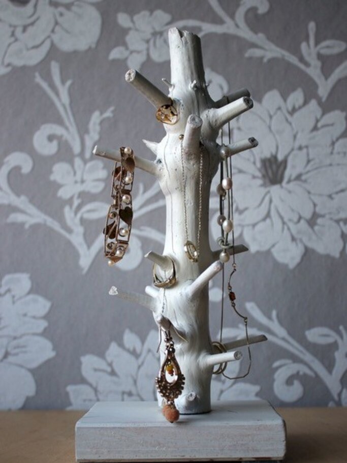 Ein weiß angestrichener Baumstamm mit Ästen auf einem Holzsockel, der Schmuck hält. | © KOLLAXO / VNWB