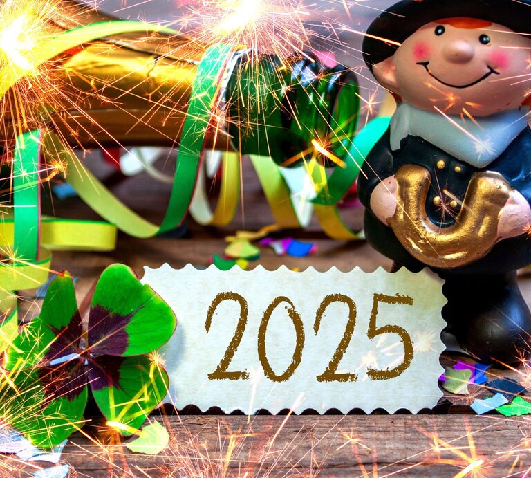 Glücksbringer-Figur mit goldenem Hufeisen, Kleeblatt, bunten Luftschlangen und Wunderkerzen vor einer Karte mit „2025“. | © Adobe Stock/Stockwerk-Fotodesign