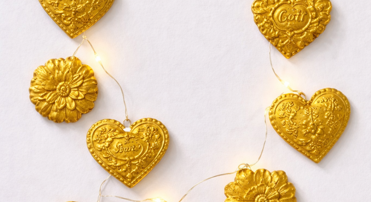 Goldene Herzen und Blumen mit Prägungen hängen an einer Lichterkette auf weißem Hintergrund in festlicher Anordnung.