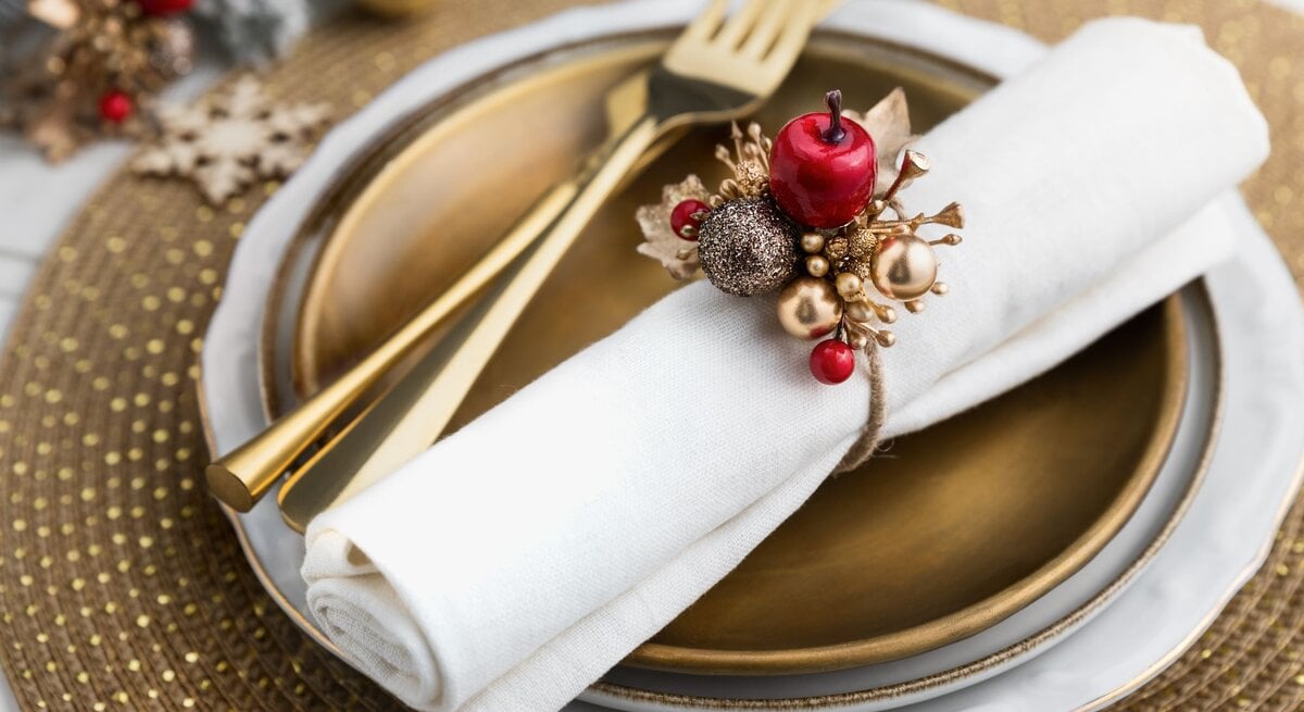 Weihnachtsdeko: Goldener Teller mit weißer Serviette und handgefertigtem Serviettenring aus glänzenden Kugeln und Beeren.