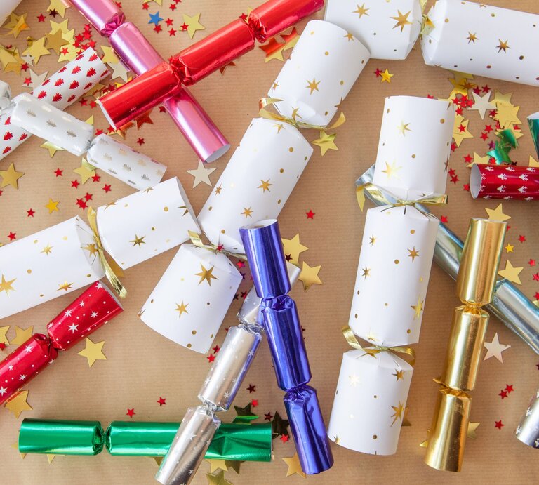 Bunte Silvester-Knallbonbons in Rot, Gold, Blau, Weiß und Grün liegen verstreut mit goldenen und roten Sternen auf braunem Papier. | © Adobe Stock/scerpica