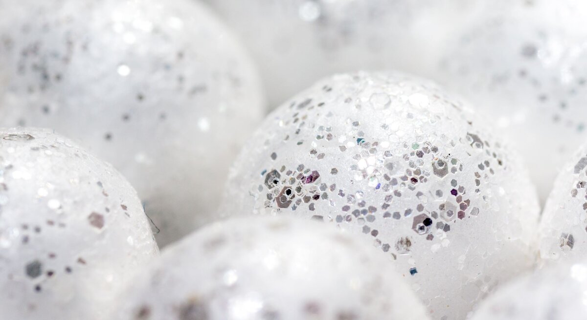 Nahaufnahme glitzernder, weißer Kugeln mit silbernen Partikeln, die Schneebälle darstellen und eine schimmernde, festliche Atmosphäre erzeugen.