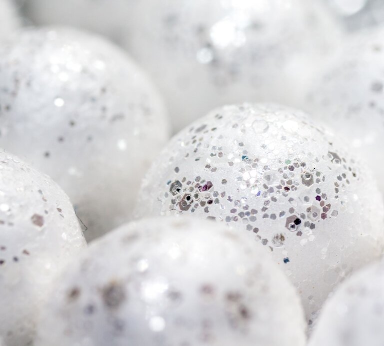 Nahaufnahme glitzernder, weißer Kugeln mit silbernen Partikeln, die Schneebälle darstellen und eine schimmernde, festliche Atmosphäre erzeugen. | © Adobe Stock/zauberblicke