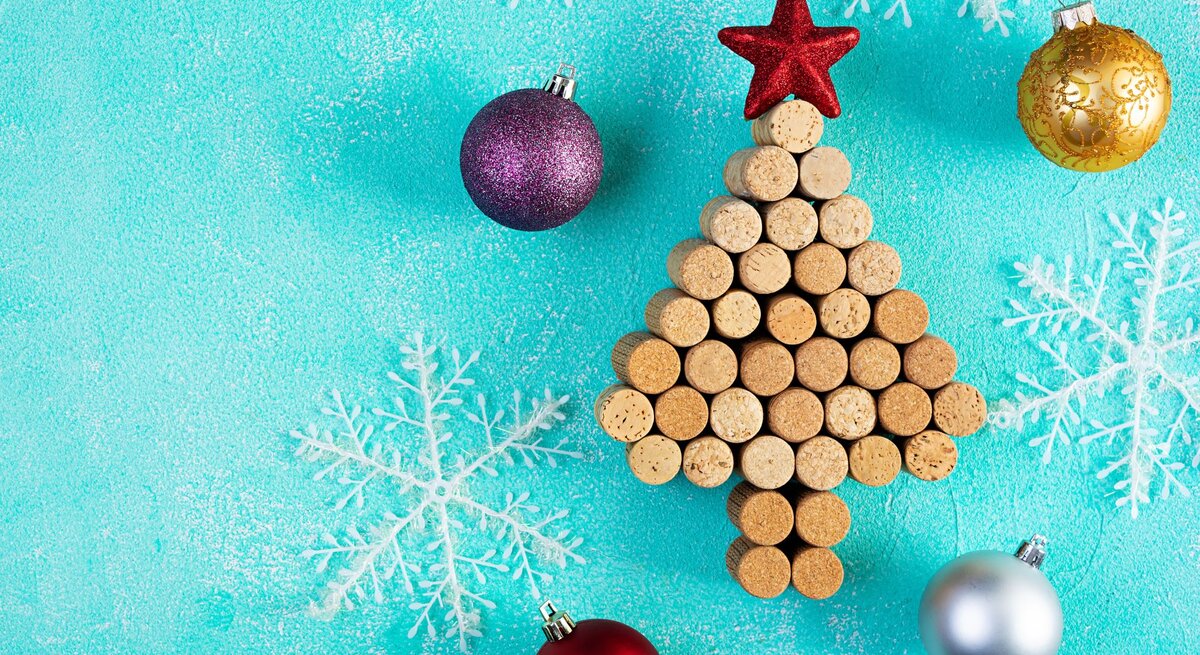 Aus Weinkorken gelegter Weihnachtsbaum mit rotem Stern, umgeben von Christbaumkugeln und weißen Schneeflocken auf türkisfarbenem Hintergrund.