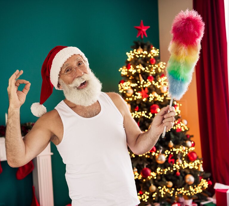 Basteln mit Staubwedel: Älterer Mann mit weißem Rauschebart und Santa-Mütze posiert lachend mit Staubwedel vor festlich geschmücktem Weihnachtsbaum. | © Shutterstock/Roman Samborskyi
