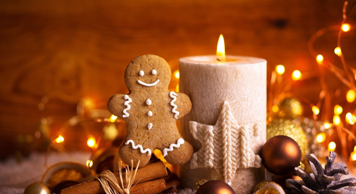 Lebkuchenmann neben einer brennenden Kerze mit Sternornament, umgeben von Zimtstangen, Tannenzapfen und weihnachtlichen Lichtern.