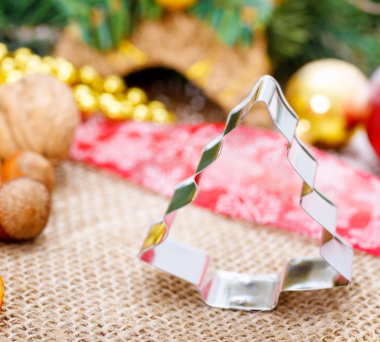 Silberne Tannenbaum-Ausstechform auf Juteunterlage, umgeben von getrockneten Orangen, Nüssen und Weihnachtsdekoration. | © Adobe Stock/Martin Rettenberger