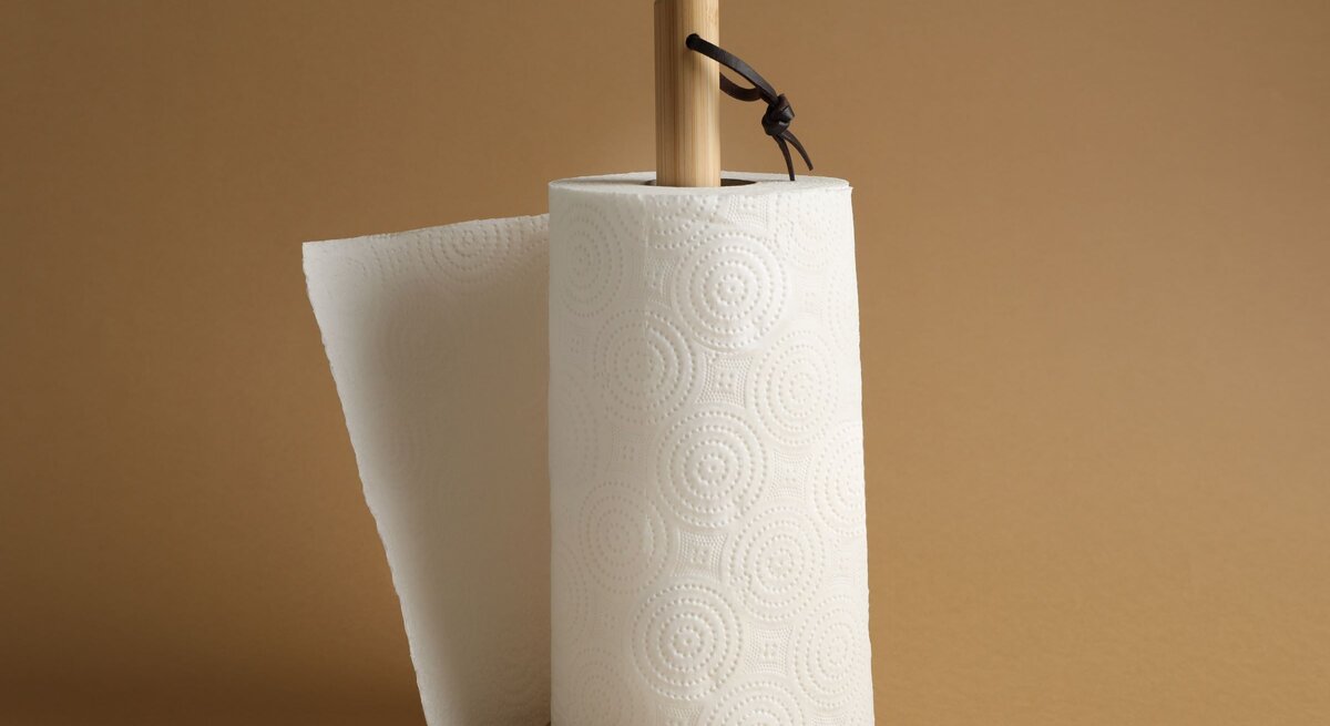 Selbst gebastelter Küchenrollenhalter aus hellem Holz mit strukturiertem Papier auf beigem Hintergrund, Blatt leicht abgerissen.