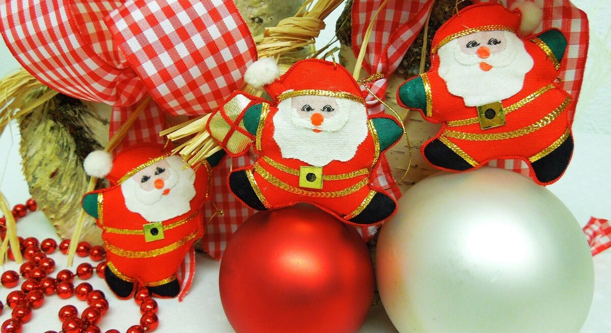 Drei Stoff-Weihnachtsmänner mit roten Anzügen hängen an einer karierten Schleife, daneben rote und silberne Kugeln.