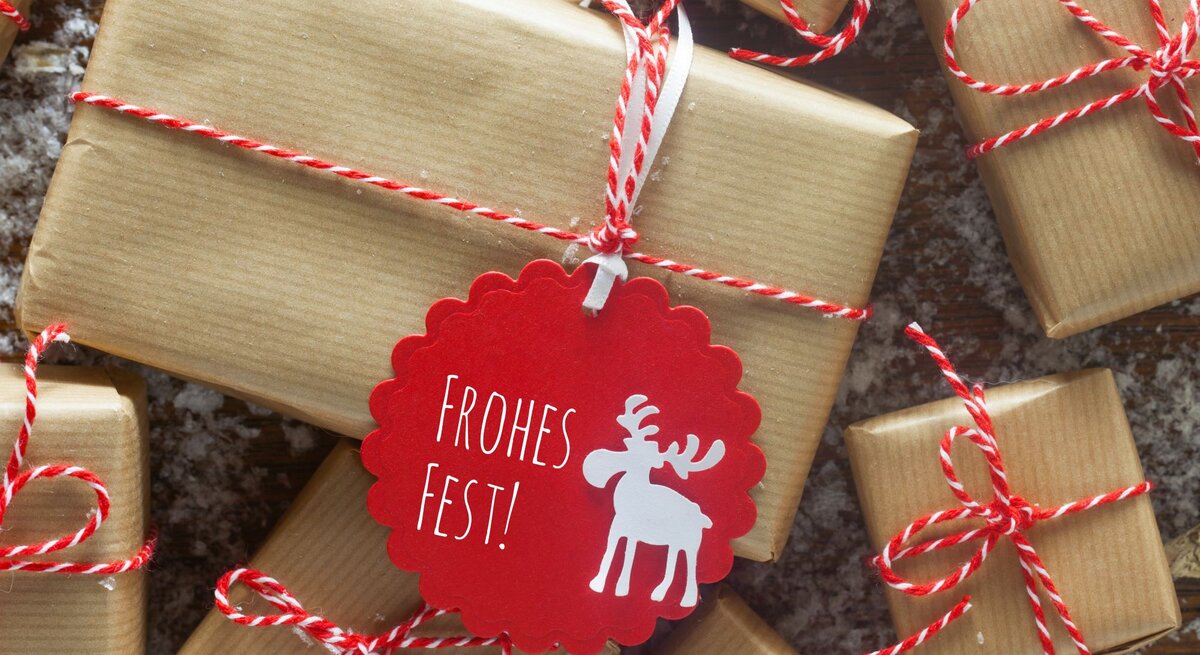 Nahaufnahme von schlichten, braun verpackten Geschenken, verziert mit roten Kordeln und einem roten „Frohes Fest“-Anhänger.