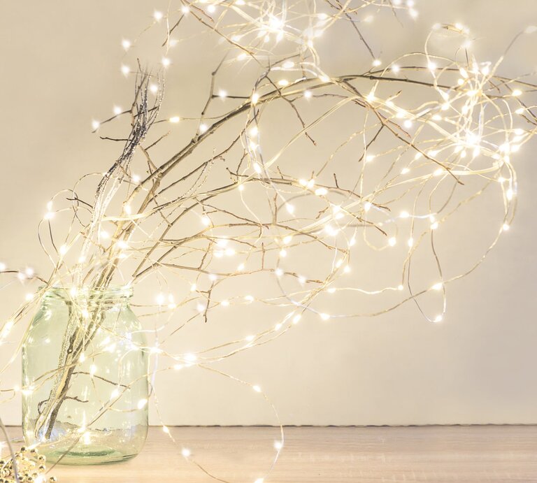 Ein bulliges glas mit Zweigen, die mit Lichterketten geschmückt sind, Hintergrund hell und die Lichterketten leuchten goldenweiss | © getty images/ stsvirkun