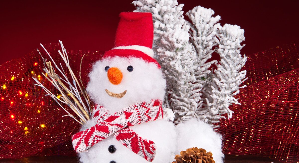 Ein lächelnder Schneemann mit rotem Hut und Schal steht vor schneebedeckten Zweigen, umgeben von roten Lichtern und einer Kiefernzapfe.