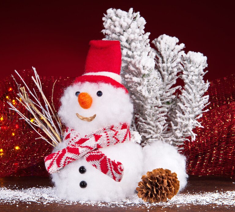 Ein lächelnder Schneemann mit rotem Hut und Schal steht vor schneebedeckten Zweigen, umgeben von roten Lichtern und einer Kiefernzapfe. | © Adobe Stock/ExQuisine