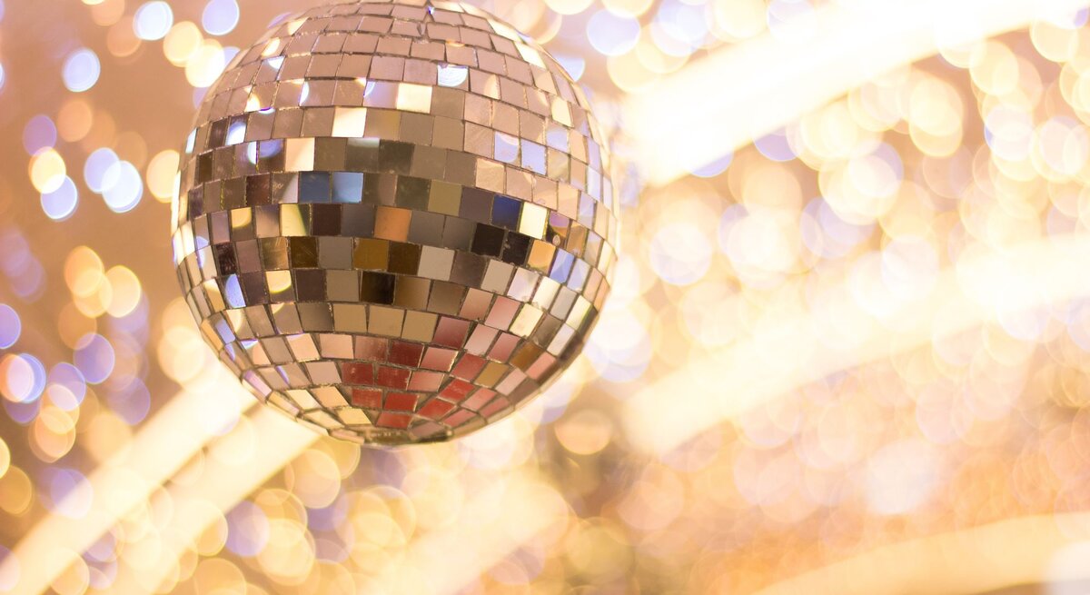 Nahaufnahme einer glitzernden Discokugel mit Spiegelmosaik, umgeben von warmen, verschwommenen Lichtreflexionen.