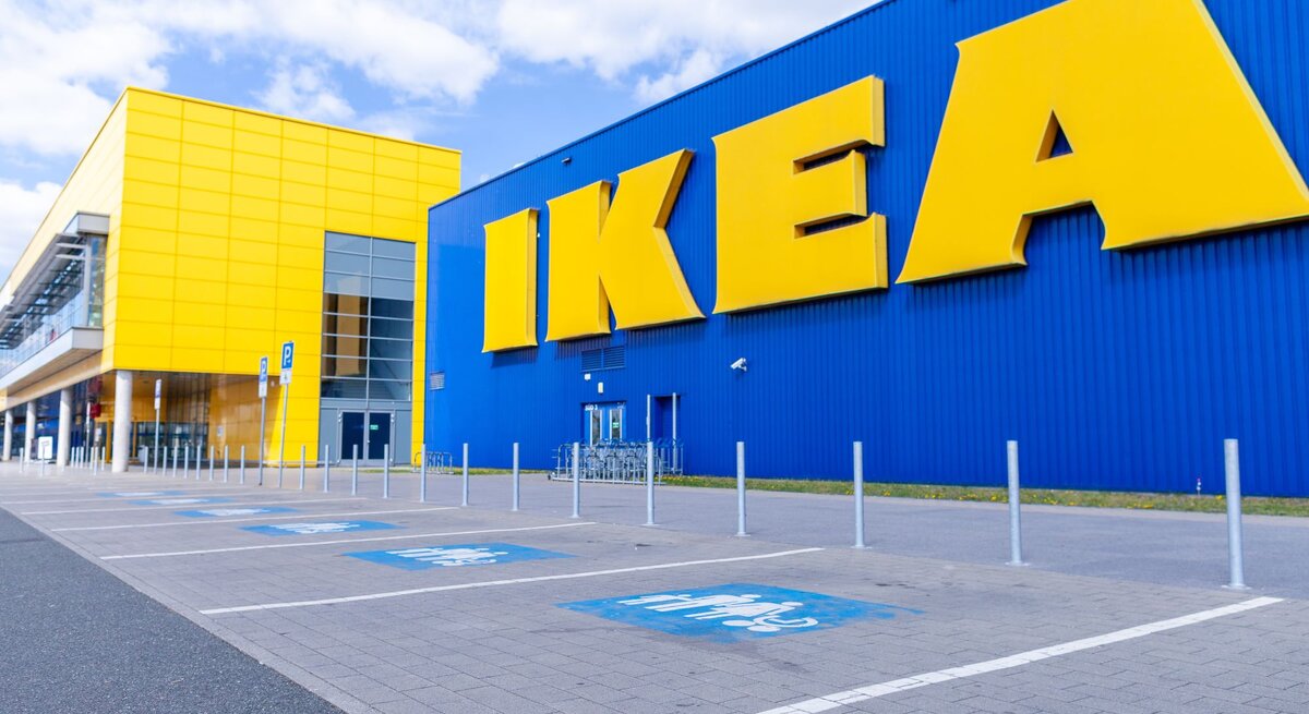 Blick auf ein modernes IKEA-Gebäude mit großer blauer Fassade und gelben Buchstaben an einem sonnigen Tag.