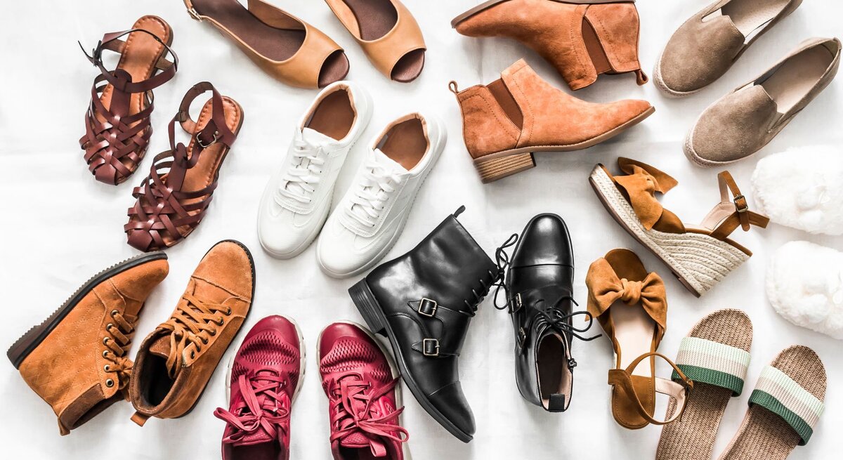 Verschiedene Schuhe wie Sneaker, Sandalen, Boots und Hausschuhe in Braun-, Rot- und Beigetönen liegen kreisförmig auf weißem Untergrund.