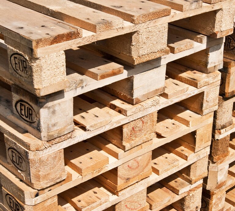 Stapel aus hellem Holz gefertigten Europaletten mit sichtbarem EUR-Logo, teils mit Gebrauchsspuren, in warmem Sonnenlicht aufgenommen. | © Adobe Stock/ PhotoSG