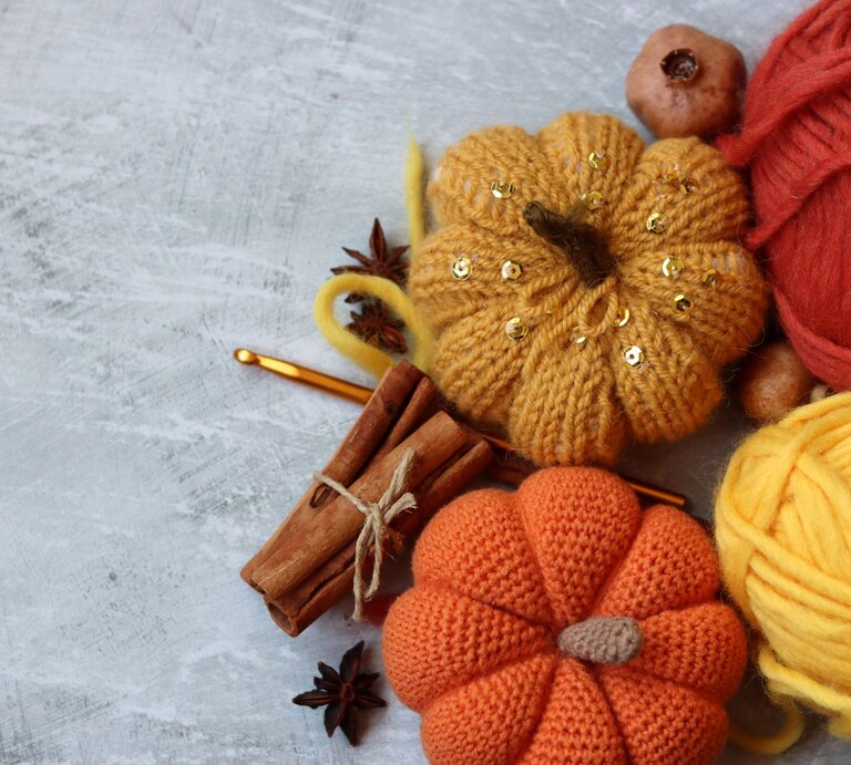 Herbstliche Deko mit orangefarbenen Häkelkürbissen, glänzender Wolle, Zimt, Sternanis und goldener Häkelnadel auf Betonhintergrund. | © Shutterstock/Maya Shustov