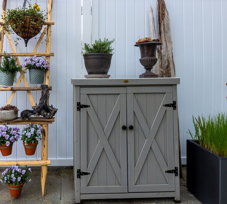 Blühende violette Blumen, Tontöpfe und Kräuter arrangiert auf Leiterregal neben rustikalem Gartenschrank aus Holz. | © Shutterstock/Jokue-photography