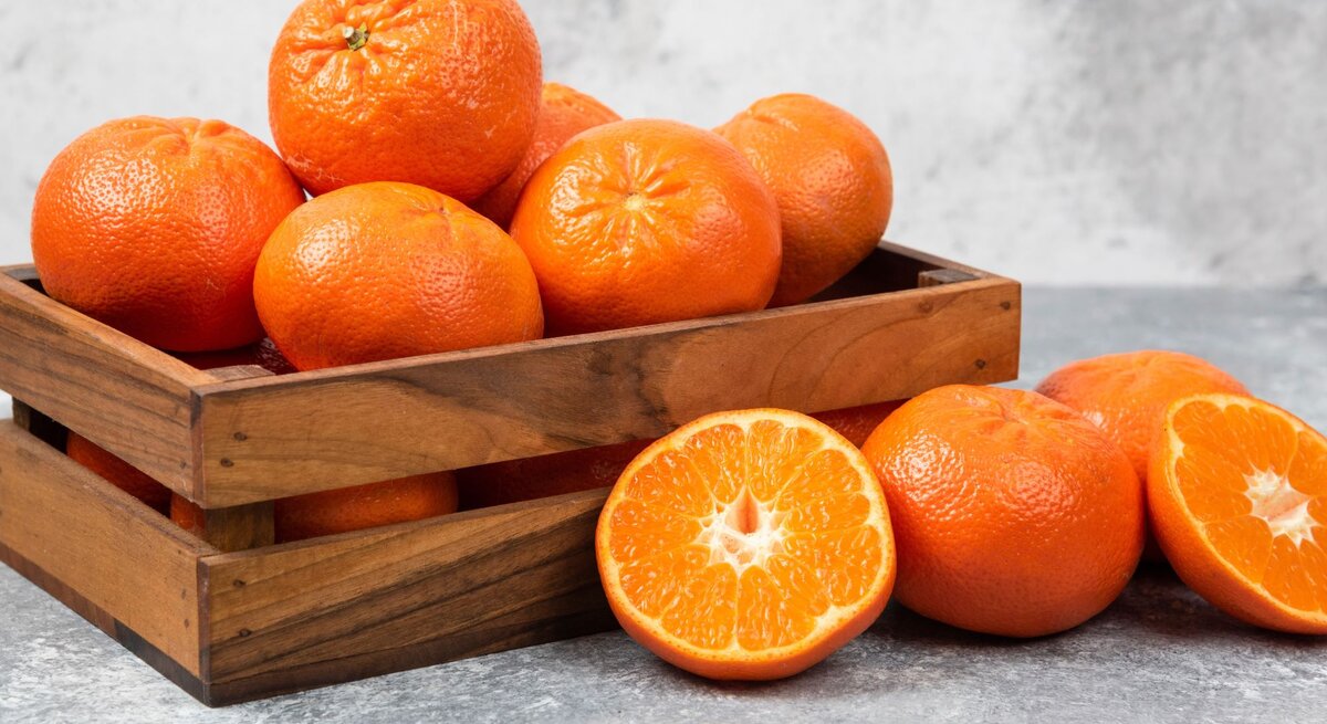 Obstkisten aus Holz mit Orangen gefüllt steht auf einem grauen Untergrund und auch der Hintergrund ist grau.