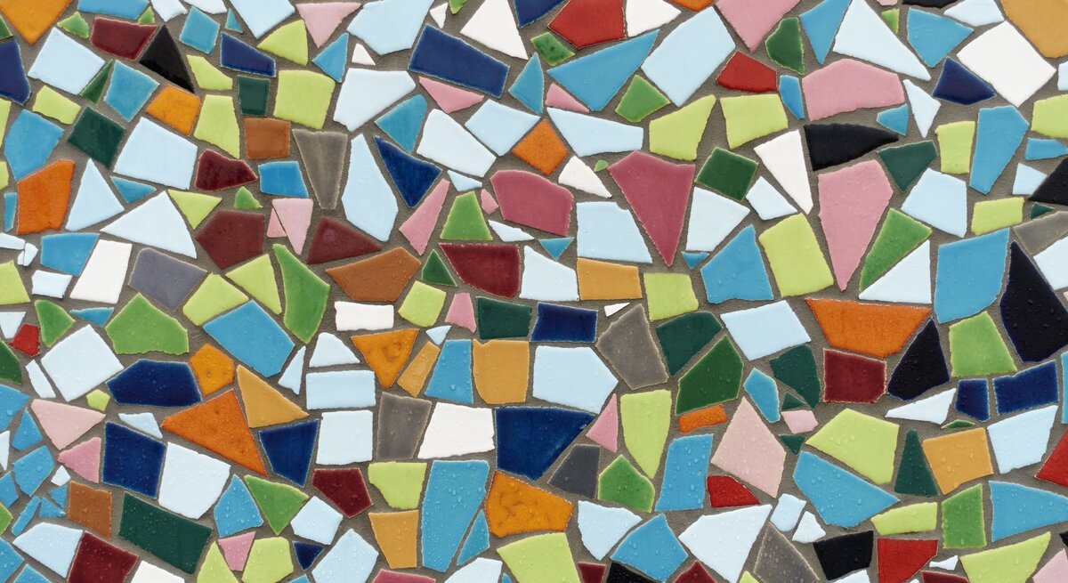 Bunte Mosaikfliesen in verschiedenen Formen und Farben sind dicht aneinandergereiht und bilden ein lebendiges, abstraktes Muster.