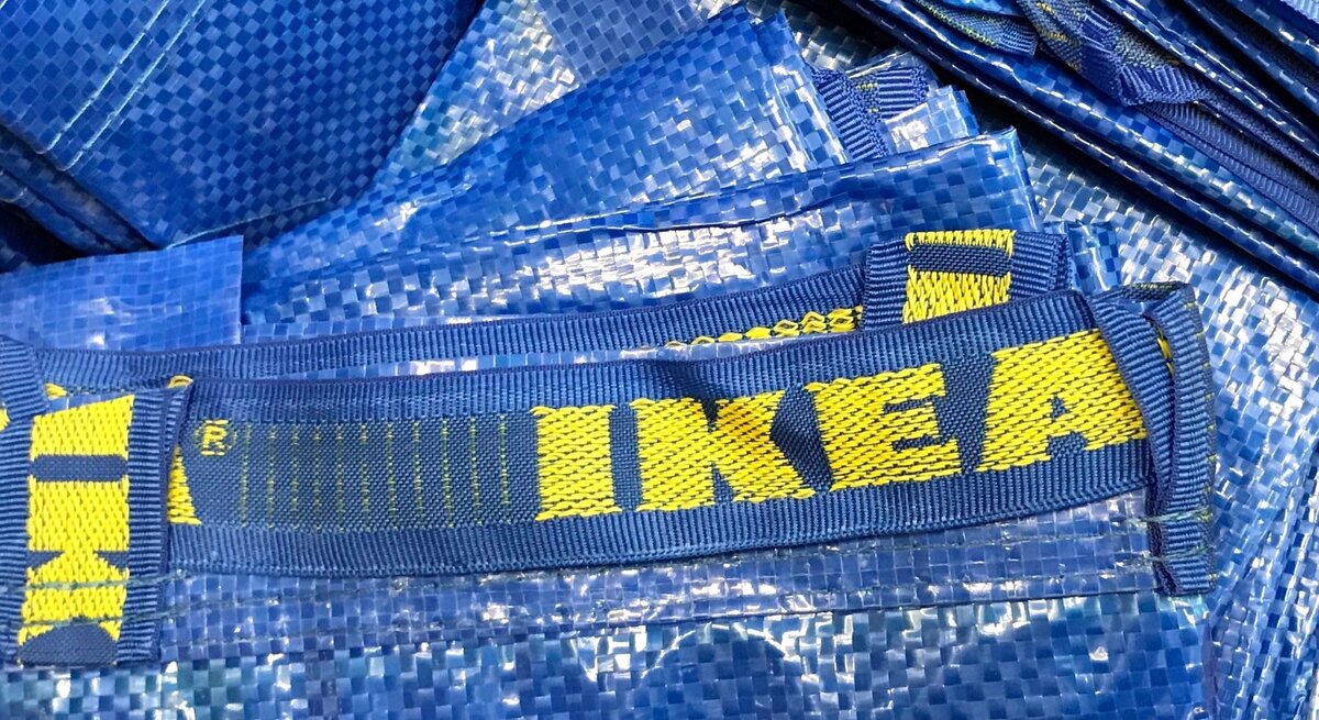 Blaue Einkaufstaschen aus Kunststoff mit gelbem "IKEA"-Logo liegen gestapelt aufeinander.