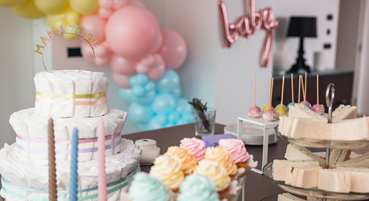 Ein Tisch mit einer Windeltorte, bunten Cupcakes, Sandwiches und Cake-Pops bei einer Babyparty mit Luftballon-Dekoration.
