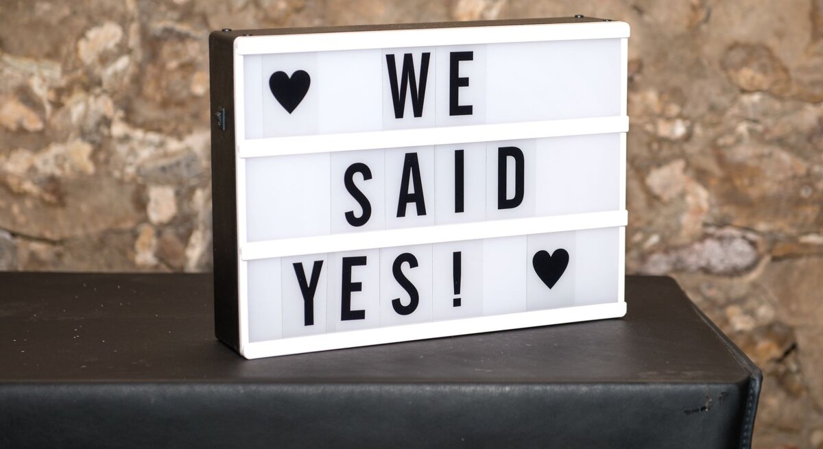 Leuchtkasten mit "We said yes!" und zwei Herzen vor einer rustikalen Steinmauer.
