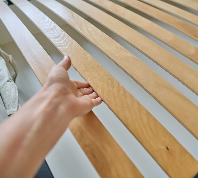 Eine Hand greift nach einer Holzlatte in einem Lattenrost, seitlich ein graues Textilband. | © Adobe Stock/Valerii Honcharuk