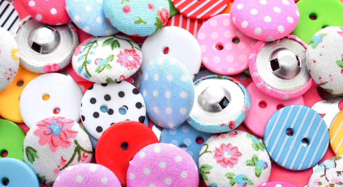 Verschiedene bunte Knöpfe mit Mustern aus Blumen, Punkten und Streifen liegen eng beieinander.