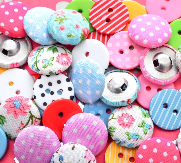 Verschiedene bunte Knöpfe mit Mustern aus Blumen, Punkten und Streifen liegen eng beieinander. | © Adobe Stock/unikat