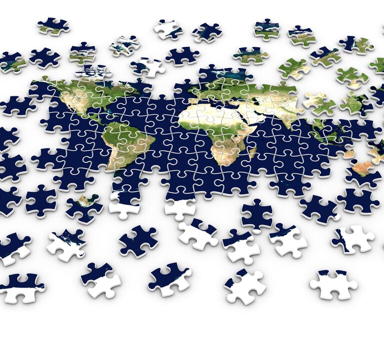 Ein teilweise fertiggestelltes Puzzle zeigt die Weltkarte mit verstreuten, noch nicht platzierten Puzzleteilen. | © Getty Images/Kuklev