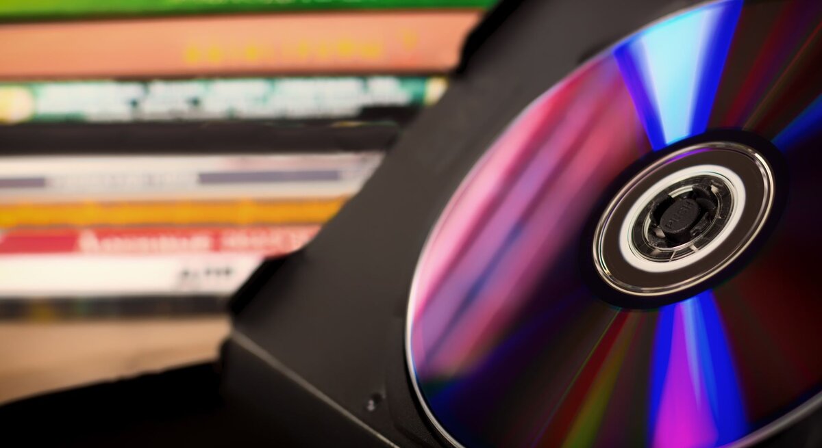 Eine glänzende CD in einer schwarzen Hülle, im Hintergrund befinden sich weitere DVDs gestapelt.