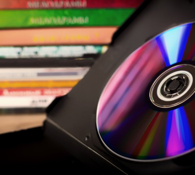 Eine glänzende CD in einer schwarzen Hülle, im Hintergrund befinden sich weitere DVDs gestapelt. | © Getty Images/Wirestock