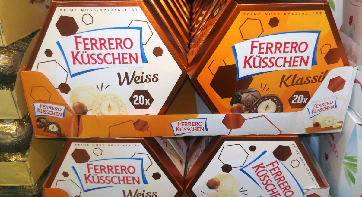 Verschiedene Sorten Ferrero Küsschen in orange-braunen Verpackungen auf einem Verkaufsdisplay im Supermarkt.