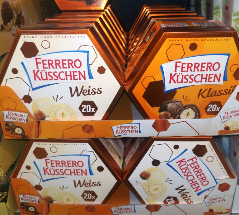 Verschiedene Sorten Ferrero Küsschen in orange-braunen Verpackungen auf einem Verkaufsdisplay im Supermarkt. | © AdobeStock/Birgit Reitz-Hofmann
