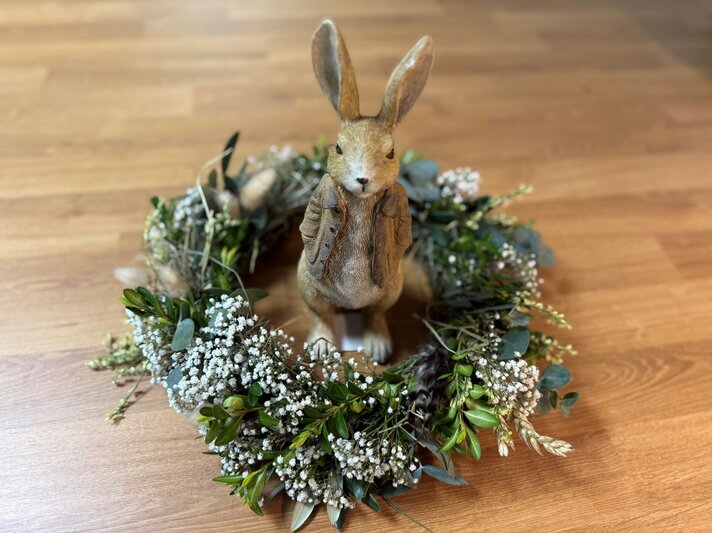 Auf Holzboden steht ein sitzender Hasenfigur mit Weste in einem Osterkranz aus Schleierkraut, Eukalyptus, Getreide und Grünzweigen. | © BILD der FRAU/Madeleine Liedke 