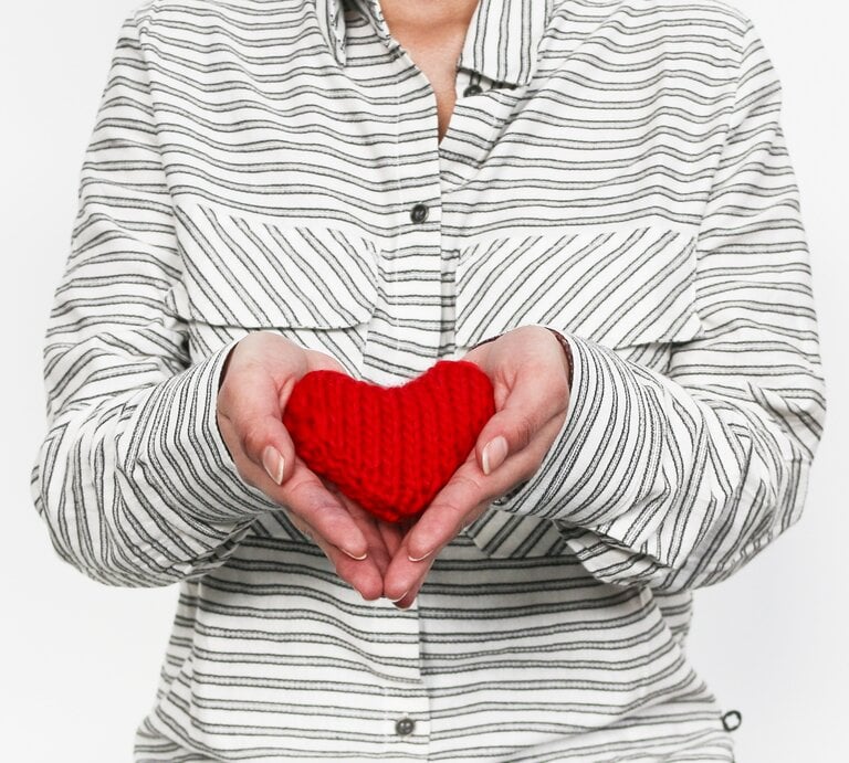 Frau hält ein rotes gestricktes Mini-Herz in ihren Händen | © we are knitters