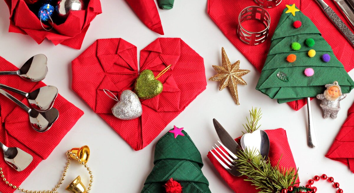 Festliche Tischdekoration mit roten Servietten in Herzform, grünen Servietten als Weihnachtsbäume gefaltet, Kugeln und goldenem Stern.
