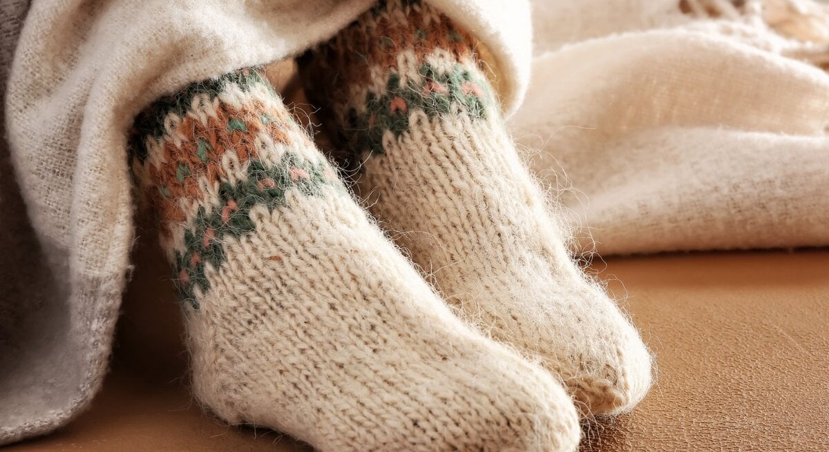 Kuschelige gestrickte Wollsocken mit farbigem Norwegermuster ragen aus beiger Decke, liegend auf einem weichen Sofa in warmem Licht.