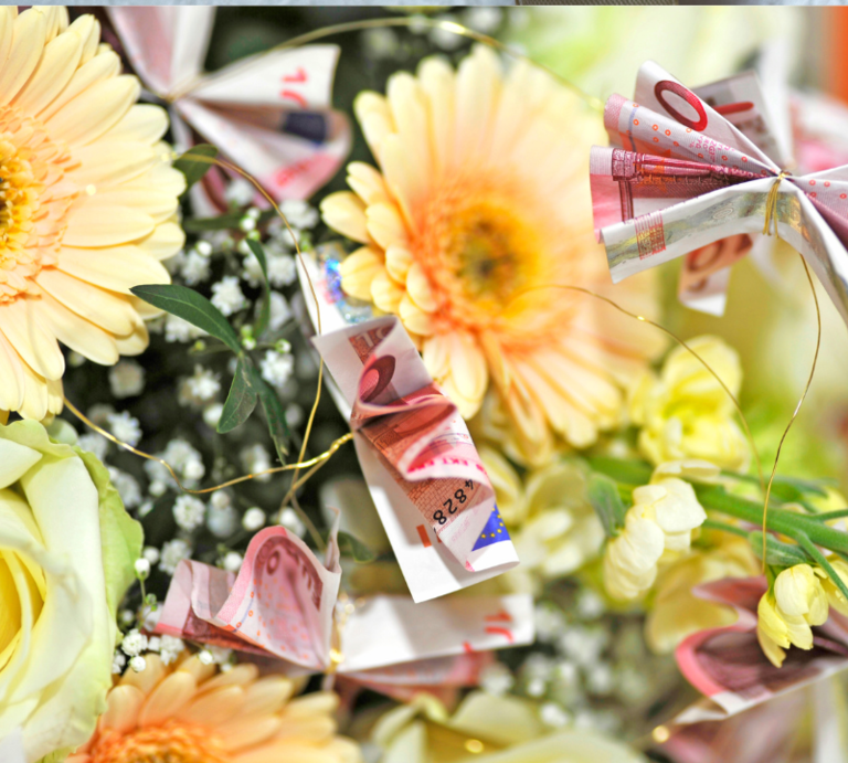 Brautpaar küsst sich unter dem Schleier, daneben ein Geldgeschenk mit Schleife und ein Blumenstrauß aus Geldscheinen und Gerbera. | © Canva/Collage:bildderfrau.de