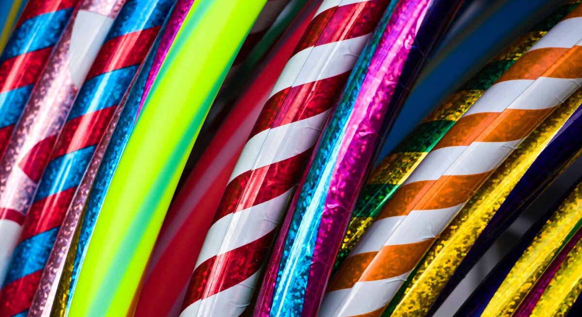 Bunte Hula-Hoop-Reifen mit glänzenden, spiralförmigen Mustern in Rot, Blau, Gelb und Neonfarben liegen dicht aneinander.