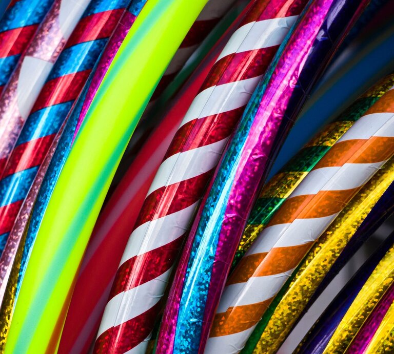 Bunte Hula-Hoop-Reifen mit glänzenden, spiralförmigen Mustern in Rot, Blau, Gelb und Neonfarben liegen dicht aneinander. | © Adobe Stock/Heike Jestram