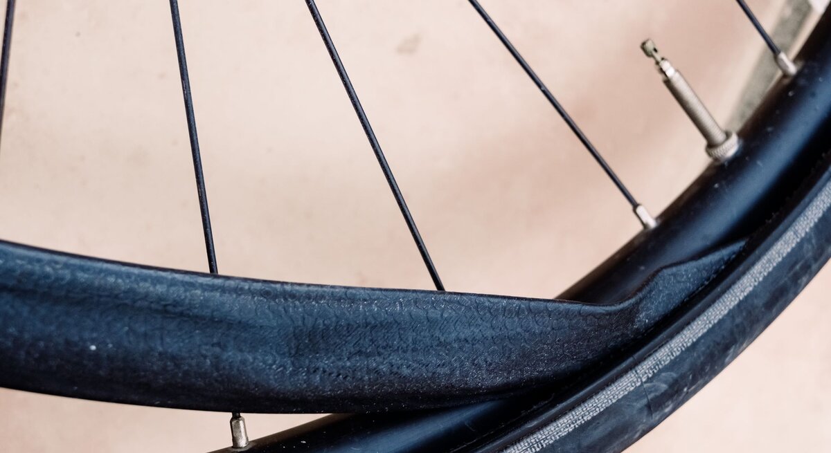 Nahaufnahme eines Fahrradreifens mit stark beschädigtem, aufgerissenem Fahrradschlauch vor hellem Untergrund.