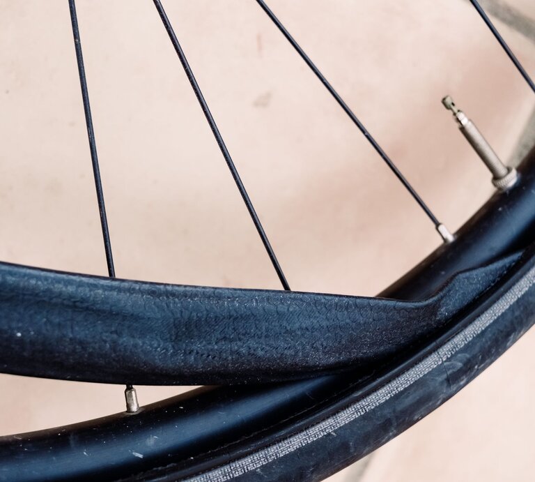 Nahaufnahme eines Fahrradreifens mit stark beschädigtem, aufgerissenem Fahrradschlauch vor hellem Untergrund. | © Adobe Stock/Joaquin Corbalan