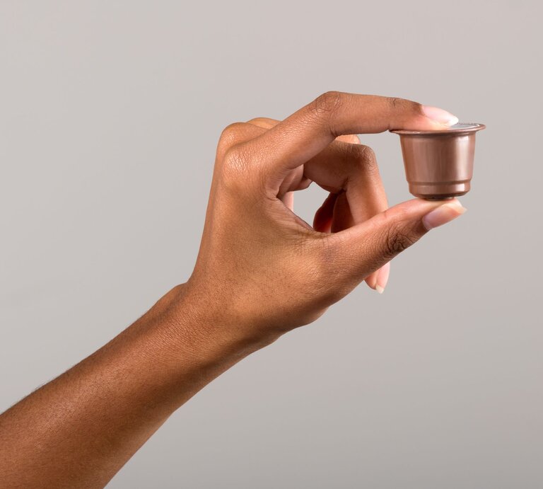  Ein Bild einer Hand, die eine gebrauchte Kaffeekapsel zwischen Daumen und Zeigefinger hält. Der Hintergrund ist einfarbig und neutral, um den Fokus auf die Kapsel zu lenken. | © Adobe Stock/photology1971