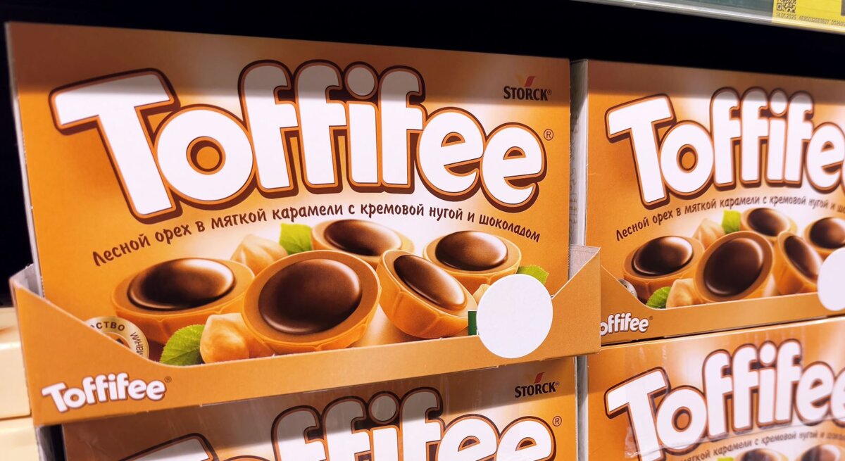 Nahaufnahme eines Supermarktregals mit orangefarbenen Toffifee-Schachteln und Preisschildern in kyrillischer Schrift.
